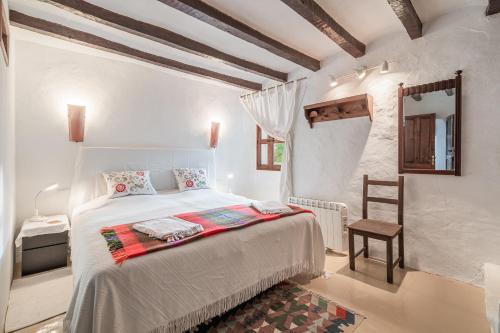 a white bedroom with a bed and a chair at Se Teulere in Fornalutx