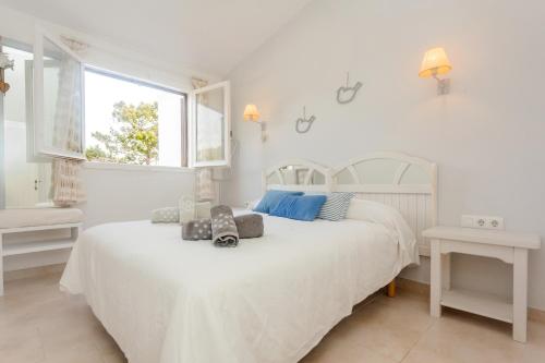 a white bedroom with a white bed and a window at El Faro 8 in Cala en Bosc