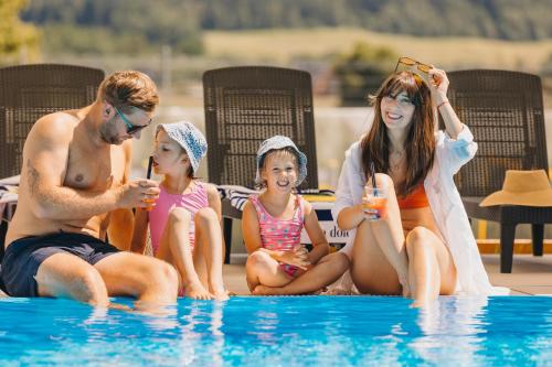 a family sitting next to a swimming pool at Osada Śnieżka koło Karpacza in Łomnica