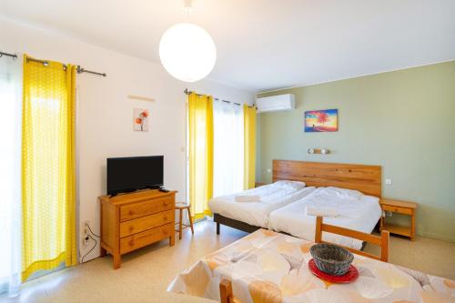 a bedroom with two beds and a tv and a table at Les Mimosas - Appartement 10 in Cazaubon