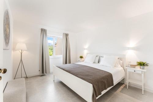 a white bedroom with a large bed and a window at Petit Paradis Apartment in Son Bou