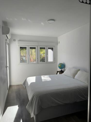 a white bedroom with a bed and two windows at Bonito bungalow en la playa in Gran Alacant
