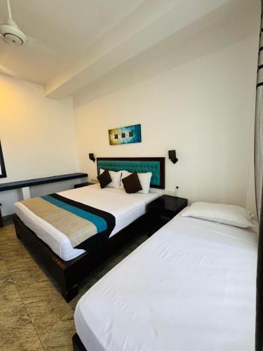 two beds in a hotel room with white walls at The Bay in Arugam Bay