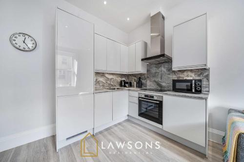 a kitchen with white cabinets and a clock on the wall at Sea You Soon I Seafront Stay in Portsmouth