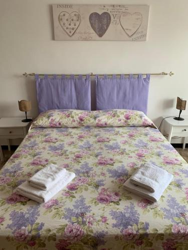 a bed with a floral bedspread and two towels on it at Serravalle Shopping - Outlet in Serravalle Scrivia