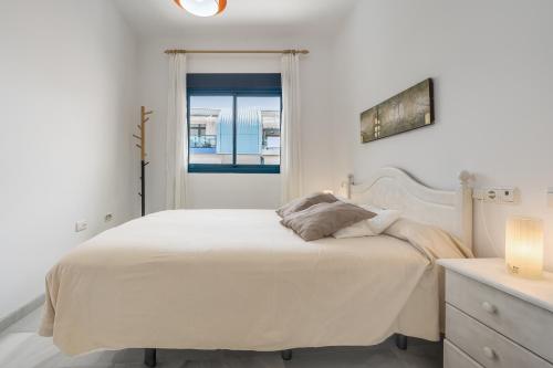 a white bedroom with a bed and a window at Piso Castell in Castell de Ferro