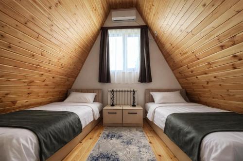 two beds in a room with wooden walls and a window at A-frame evlər-II in Qusar