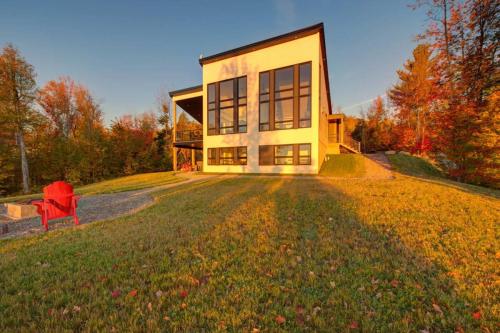 a large house with a red chair in front of it at O Vitre Spa - Relax with St-Lawrence Views in Les Éboulements