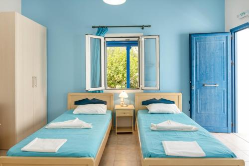 two beds in a room with blue walls and a window at Studios Ninemia Serifos 3 in Livadi
