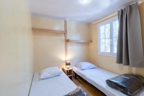 two beds in a room with a window at Mobilhome Calvi 15 Climatisé in Bouzic