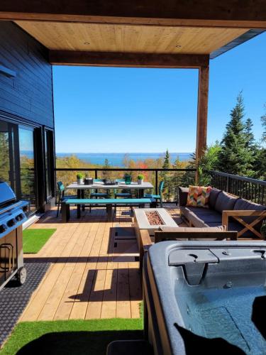 a deck with a hot tub and a patio with a table at Chalet Le Select - Private Spa with River View in Les Éboulements
