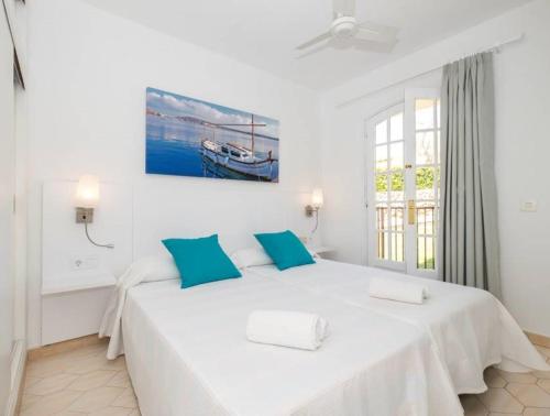 a white bedroom with a large bed with blue pillows at Girasol Garden Superior 2-b in Menorca
