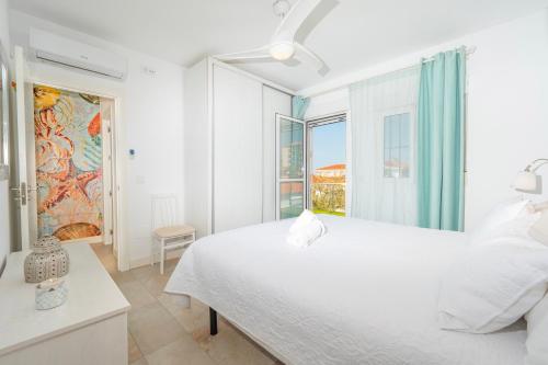 a white bedroom with a large bed and a window at Precioso chalet a pie de playa in Punta Umbría