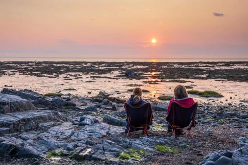 two people sitting in chairs watching the sunset on the beach at Chalet Le Pointu - St-Lawrence River View in Rivière-du-Loup