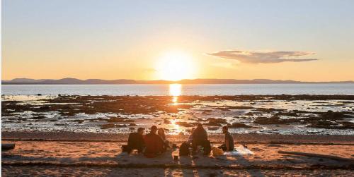a group of people sitting on the beach watching the sunset at Chalet Le Pointu - St-Lawrence River View in Rivière-du-Loup