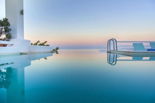 a swimming pool with two chairs in the water at Anema Boutique Hotel & Villas Santorini in Vourvoúlos