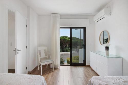 a white bedroom with a mirror and a chair at Pear Tree Villa in Vale do Lobo
