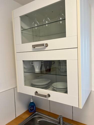 a white cabinet with dishes in it next to a sink at Apartments Neckarsulm in Neckarsulm