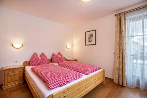 a bedroom with a bed with red pillows and a window at Ciasa Tlara App Lisa in San Vigilio Di Marebbe