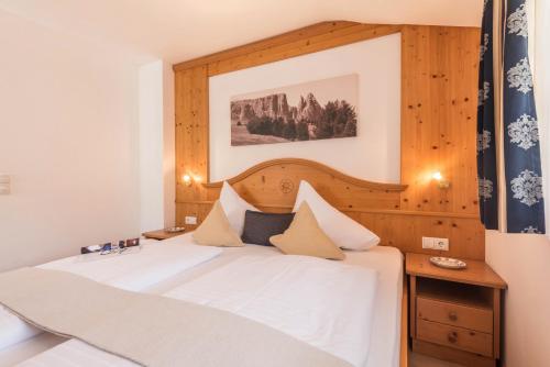 a bedroom with a white bed with a wooden headboard at Kristiania Apartement Typ A2 in Siusi