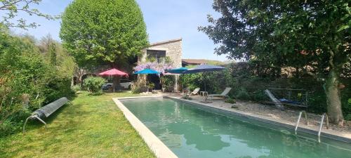 a swimming pool in a yard with two umbrellas at Au fil de l'eau in Chambonas