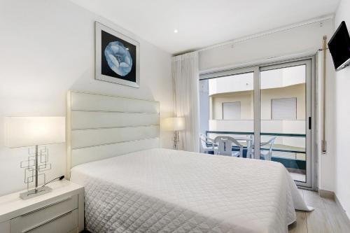 a white bedroom with a bed and a window at Natalina T2 in Nazaré