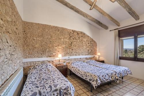 a bedroom with two beds and a stone wall at Cal Cabrer in Sant Jaume dels Domenys