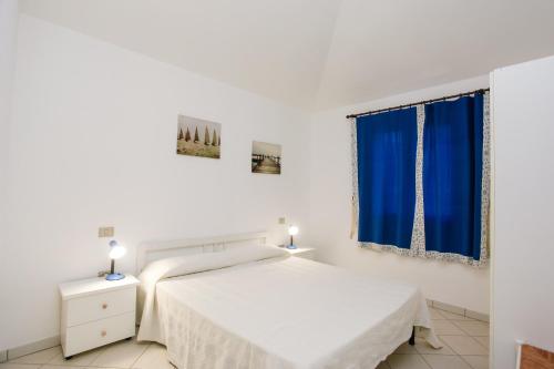 a white bedroom with a bed and blue curtains at mirtagru appartamento dell'oleandro in Budoni