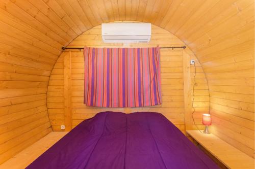 ein lila Bett in einem Holzzimmer mit Fenster in der Unterkunft Barrel Violet in Saint-André