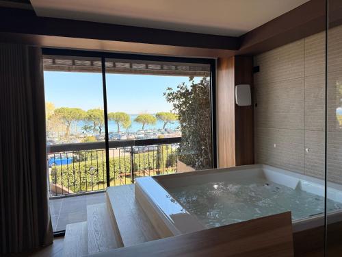 a bath tub in a room with a large window at Alevic Hotel Sirmione in Sirmione