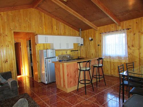 a kitchen with a refrigerator and a counter with stools at Cabañas Entremontañas Coñaripe in Coñaripe