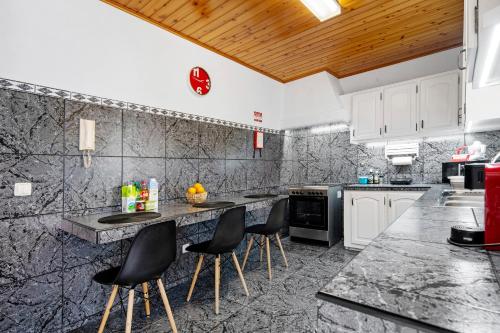 a kitchen with marble counter tops and black chairs at Casinha do Monte in Achadinha
