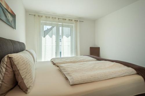 a white bedroom with a bed and a window at Fink - Vogelhaus in Friedrichshafen