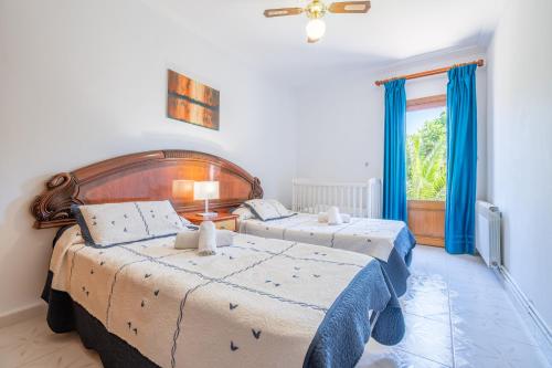 a bedroom with two beds with blue curtains and a window at Villa Juana Maria in Cala Murada