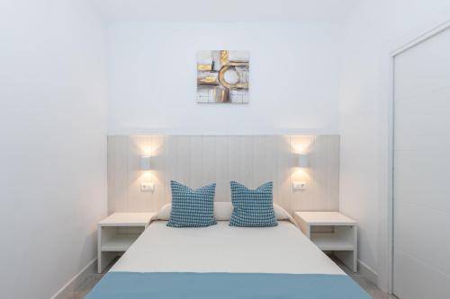 a bedroom with a white bed with blue pillows at Victoria's Apartamentos Beach in Málaga