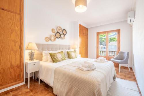 a white bedroom with a bed and a chair at Voramar Alcudia in Alcudia