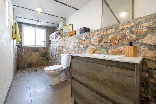a bathroom with a toilet and a stone wall at Beach house in Torredembarra