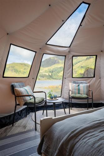 a tent with two chairs and a bed and windows at FLO Lofoten nature escape in Valberg