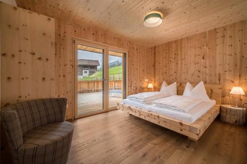 a bedroom with a bed and a chair and a window at Naturapartments Alpreid Zirbe in San Pancrazio dʼUltimo