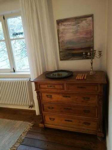 a dresser with a clock on top of it next to a window at Ludwig im Künstlerhaus in Langmühle