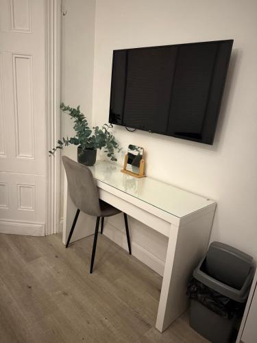 a white desk with a chair and a television on a wall at Seaside studio apartment in Weston-super-Mare