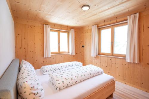 a bed in a wooden room with two windows at Haus Hoalp in Au
