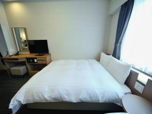 a hotel room with a white bed and a television at Dormy Inn Akihabara in Tokyo