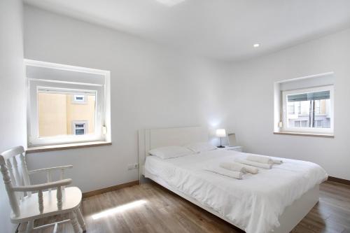 a white bedroom with a bed and a chair at Casa Ribeiro Alojamento Local in São Martinho do Porto