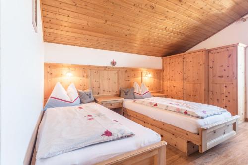 two beds in a room with wooden walls at Schildberghof Schlernblick in Kastelruth