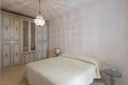 a white bedroom with a bed and a chandelier at Elegant Central Large House F1F2 in Gravedona