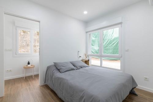 a white bedroom with a bed and two windows at Aptos Ría San Cosme Aurora in Bendimón