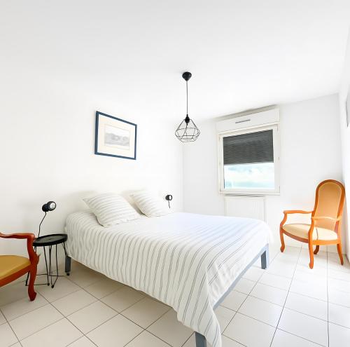 a white bedroom with a bed and two chairs at Appartement De Standing Avignon in Avignon