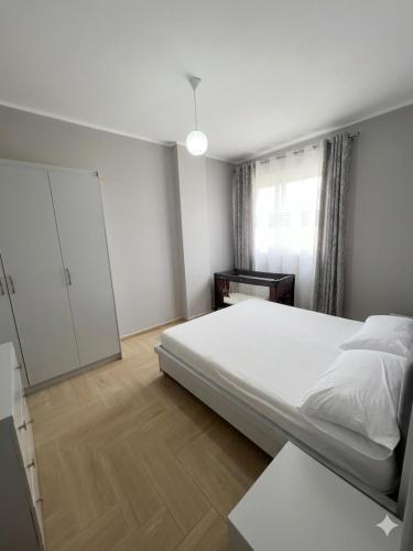 a white bedroom with a bed and a window at Radhima Beach Apartments in Vlorë
