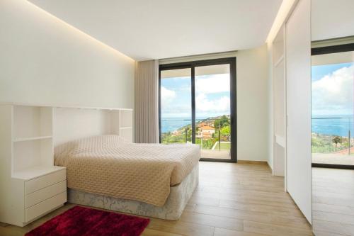 a white bedroom with a bed and large windows at Casa Jolie in Ponta do Sol